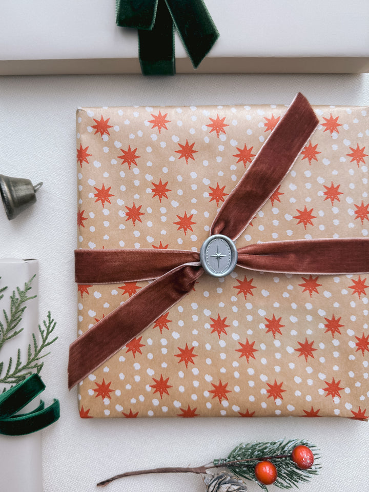 Silver mini oval 3D North star wax seal on a star-patterned festive gift wrap tied with a brownish red velvet ribbon