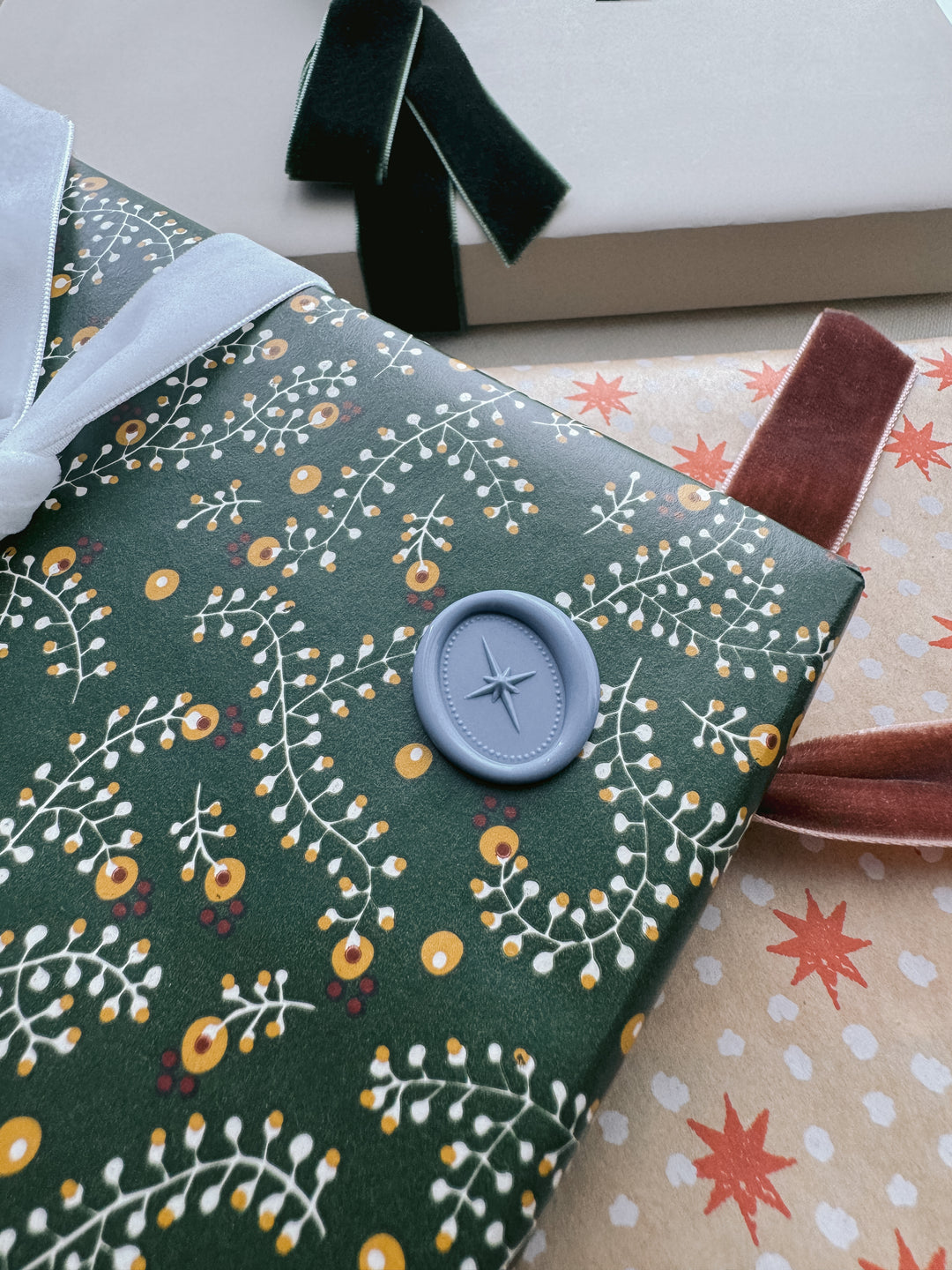 Dusty blue oval 3D star motif wax seal on a dark green botanical festive gift wrap 