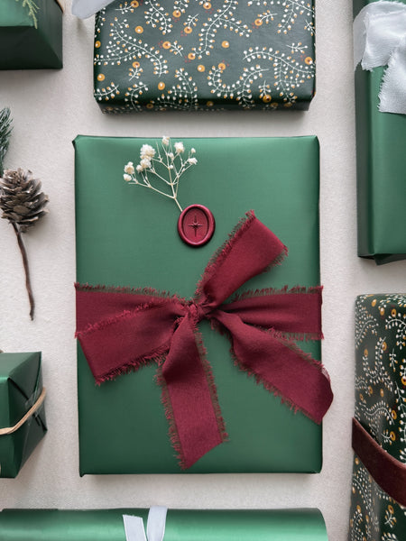 dark metallic red North Star wax seal on a wrapped Christmas gift with red silk ribbon tied around the gift