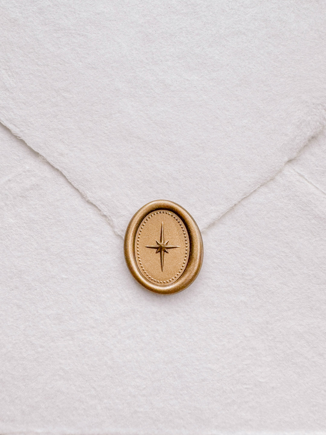 Gold mini oval 3D North star wax seal on a  white deckle-edge handmade paper envelope