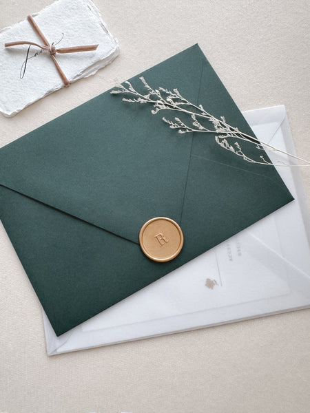 light gold colored personalized initial wax seal on a dark green envelope