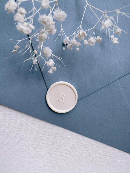 off-white custom letter wax seal on a dusty blue envelope