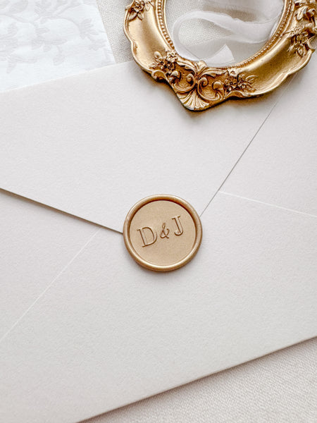 Modern typeface monogram light gold wax seal on a beige envelope