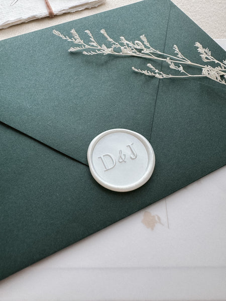 Modern typeface monogram wax seal in white pearl color on a dark green envelope