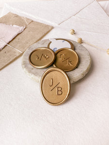 Oval monogram custom wax seals in gold styled with a small gray stone dish, handmade paper and a dried floral branch