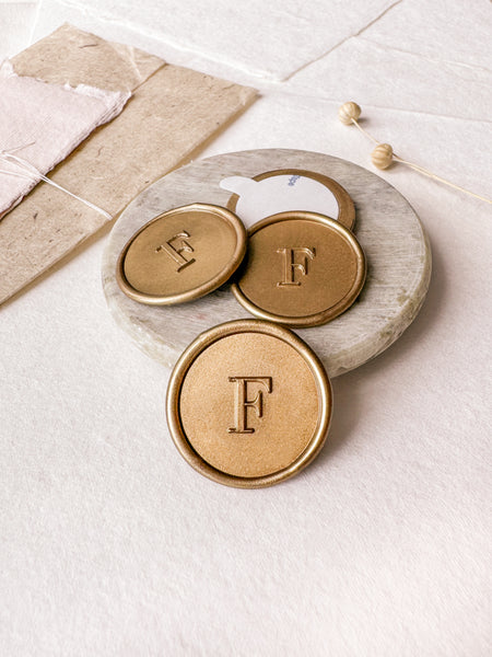 Single initial monogram round custom wax seals in gold styled with a small gray stone dish, handmade paper and a dried floral branch