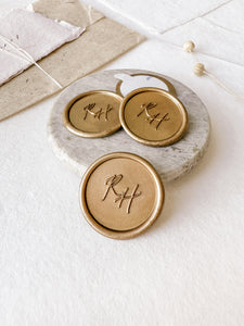 Monogram round custom wax seals in gold styled with a small gray stone dish, handmade paper and a dried floral branch