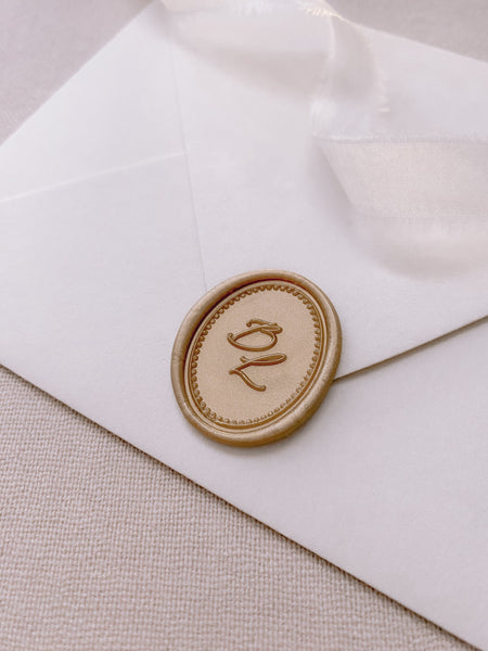 Calligraphy script monogram with border design oval light gold custom wax seal in on white paper envelope styled with a strand of white silk ribbon