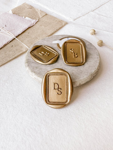 Border monogram rectangular custom wax seals in gold styled with a small gray stone dish, handmade paper and a dried floral branch