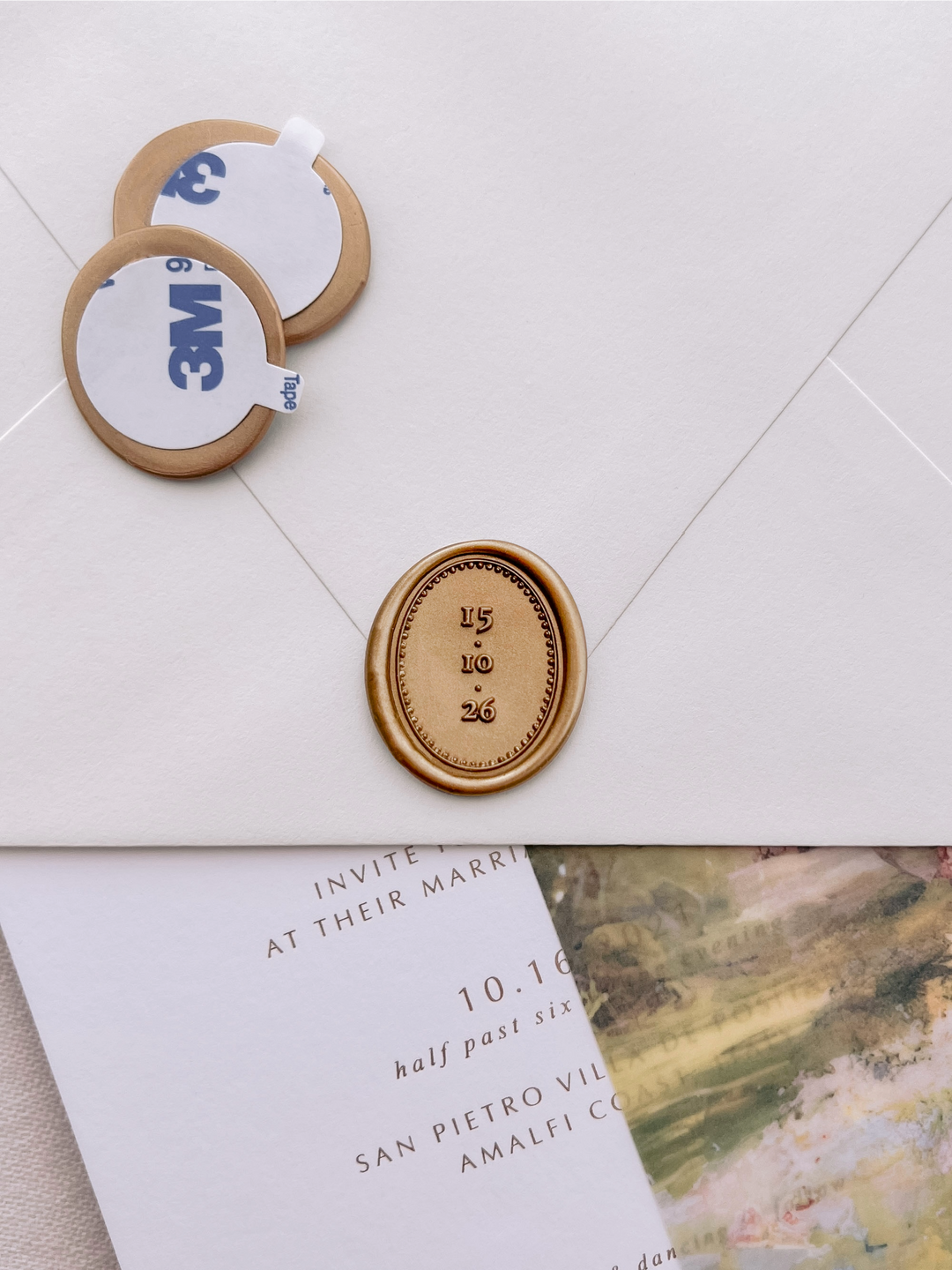 Gold custom wedding date oval wax seal stickers with self-adhesive backings on a wedding invitation, beige envelope, and vellum jacket