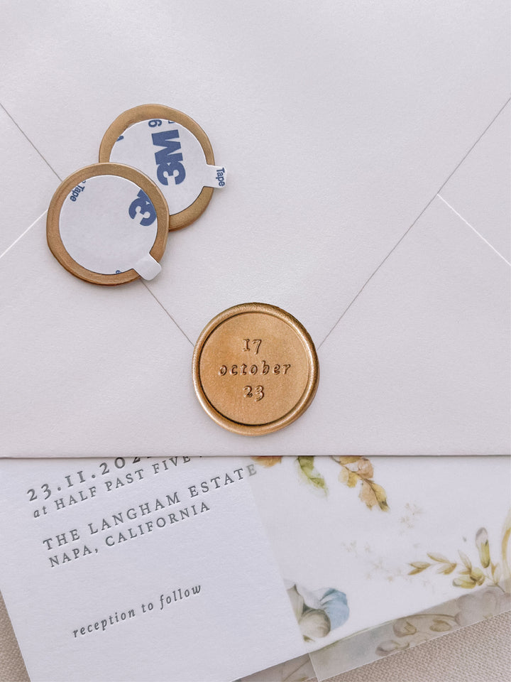 custom date classic gold wax seal stickers with self-adhesive backings on a wedding invitation, beige envelope, and floral vellum jacket