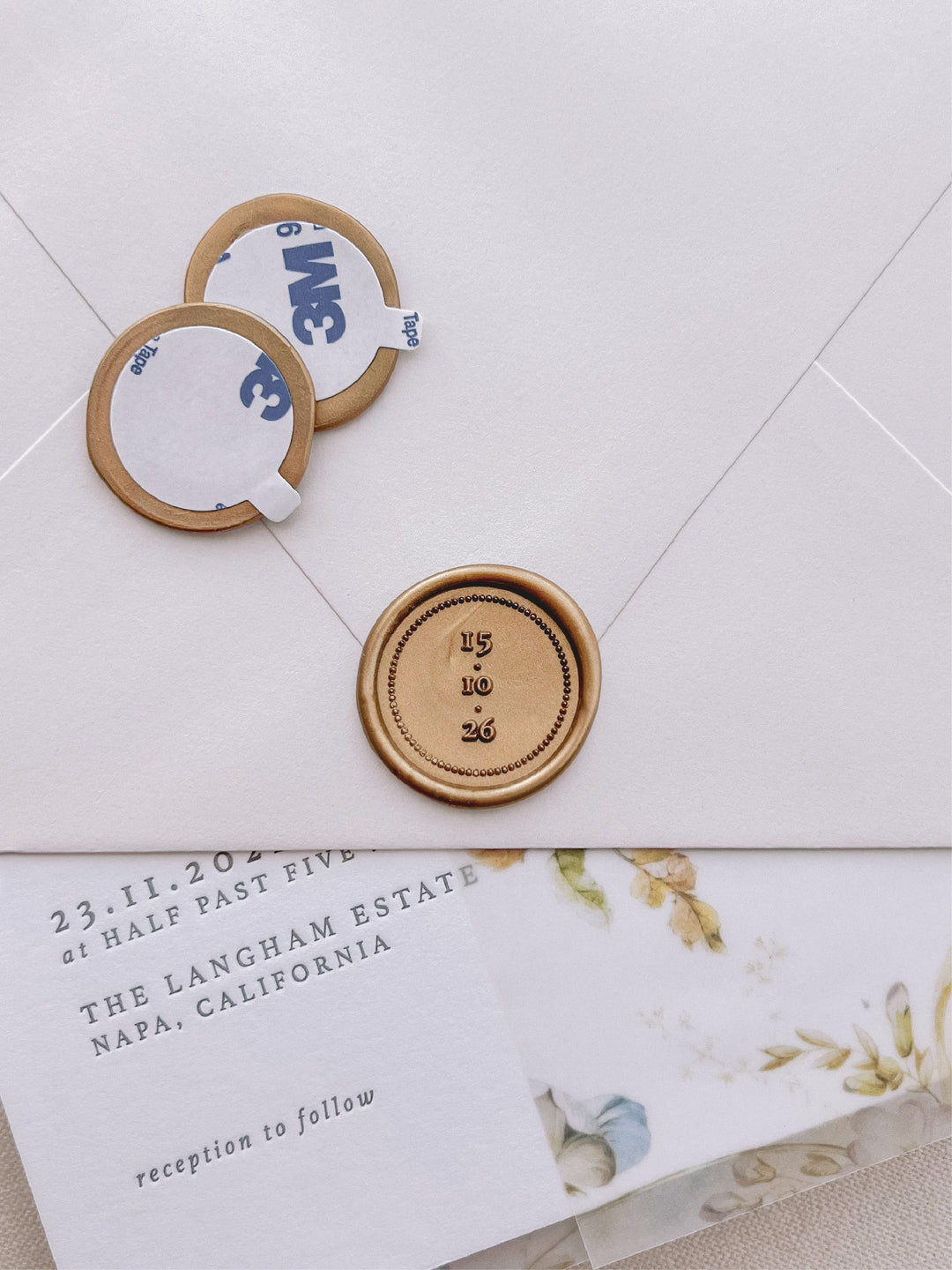 Custom wedding date gold wax seal stickers with self-adhesive backings on a wedding invitation, beige envelope, and vellum jacket