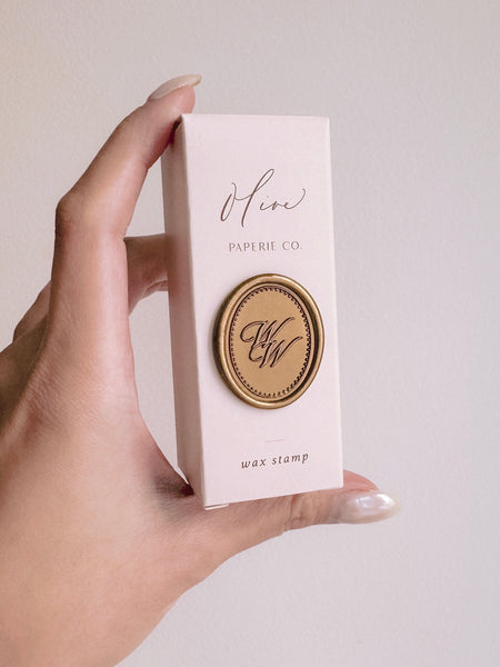 Custom monogram oval gold wax seal attached on a beige packaging box