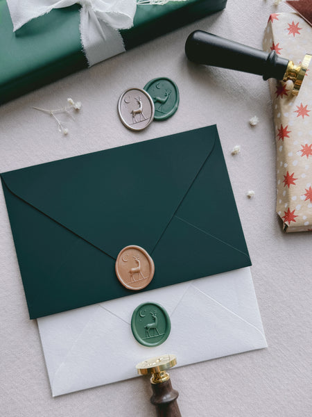 gold and green reindeer wax seals on dark green and white envelopes 