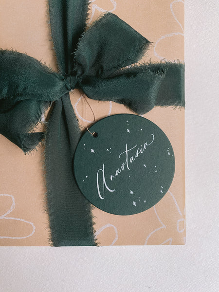 Christmas gift wrapped in dark green silk ribbon decorated with personalized round gift tag