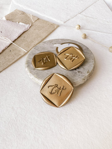 Monogram diamond custom wax seals in gold styled with a small gray stone dish, handmade paper and a dried floral branch