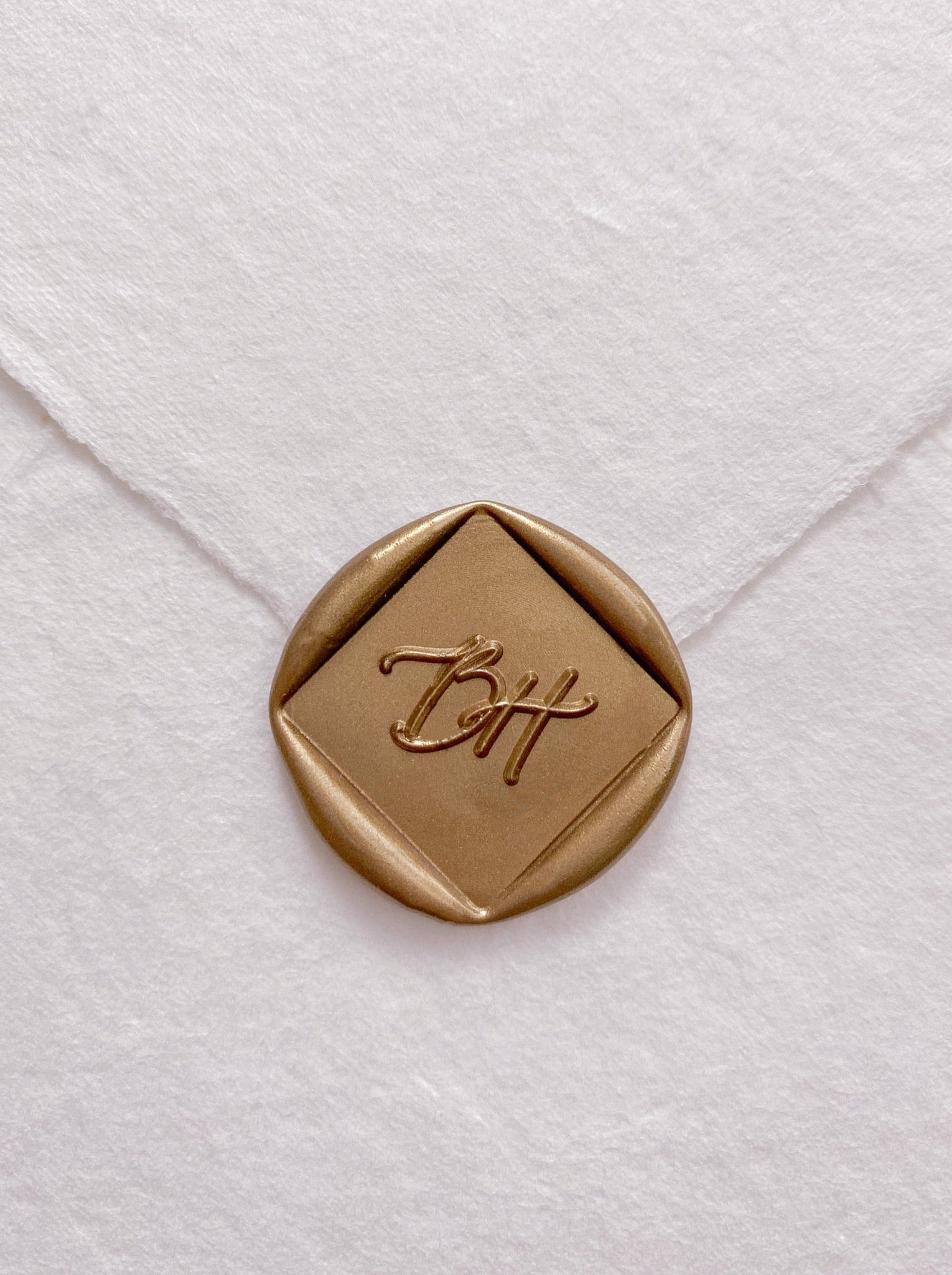 Calligraphy script monogram diamond shaped wax seal in gold on handmade paper envelope