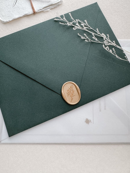 Oval arch shaped leaf design gold wax seal on a dark green wedding invitation envelope