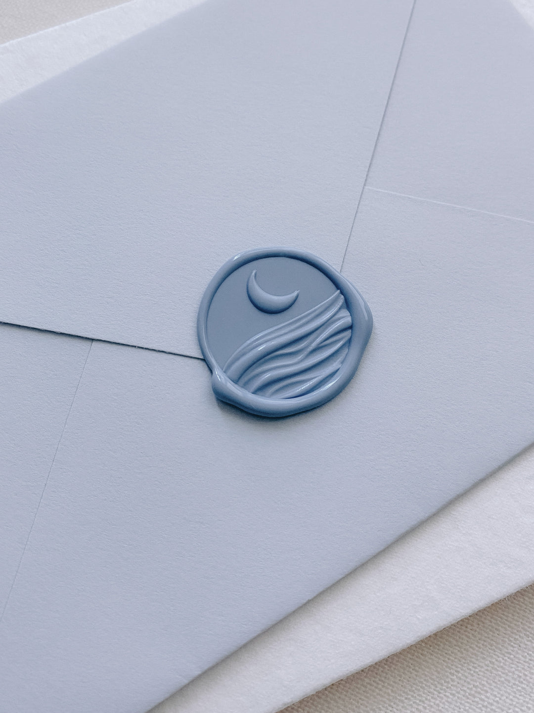 Moon and ocean waves with 3D engraving wax seal in dusty blue on light blue paper envelope