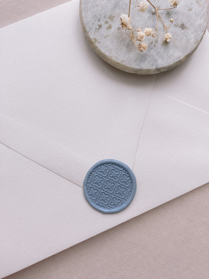 Moroccan tile pattern wax seal in dusty blue on beige paper envelope styled with small gray stone dish and dried flowers