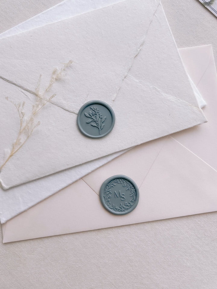 teal colored eucalyptus bouquet wax seal and custom monogram wax seal on white and beige envelopes