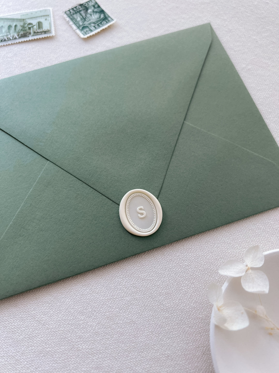 off-white custom letter mini oval wax seal on an olive green envelope