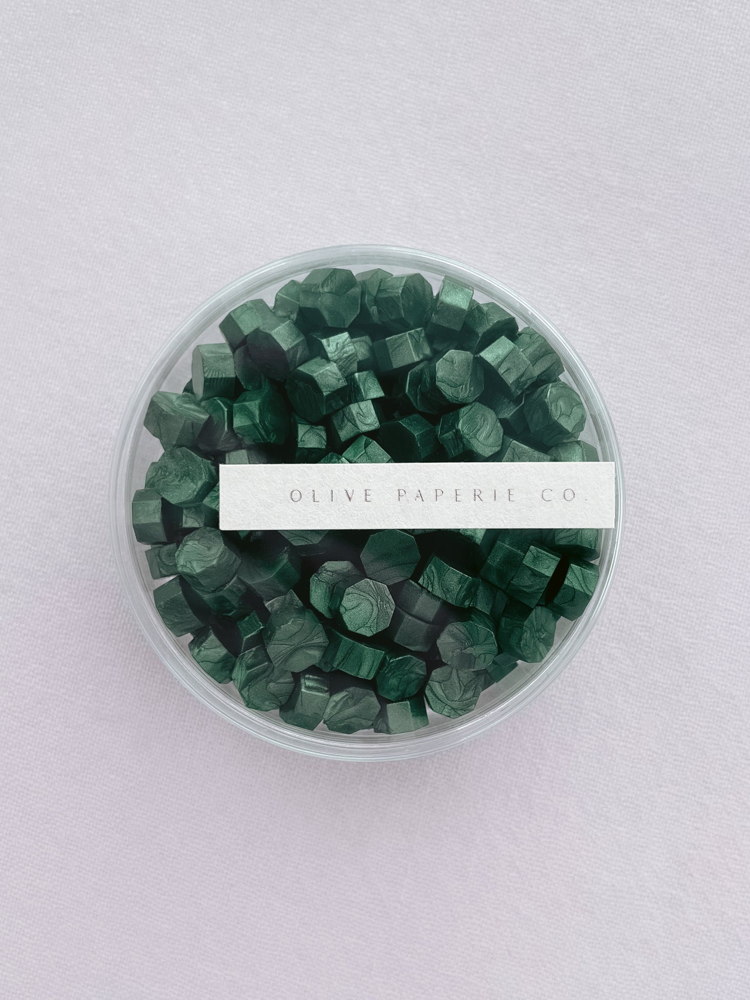 Metallic green sealing wax beads in a clear round container