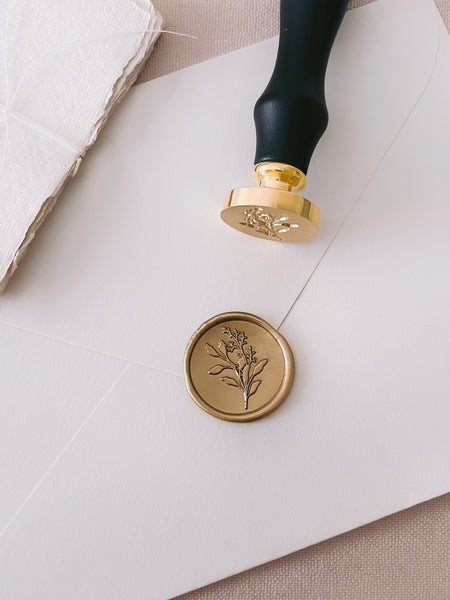 Gold eucalyptus leaf gold wax seal on beige envelope with wax seal stamp placed on top of envelope
