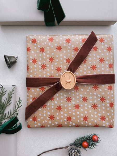 Gold reindeer oval wax seal on a wrapped Christmas gift with velvet ribbon