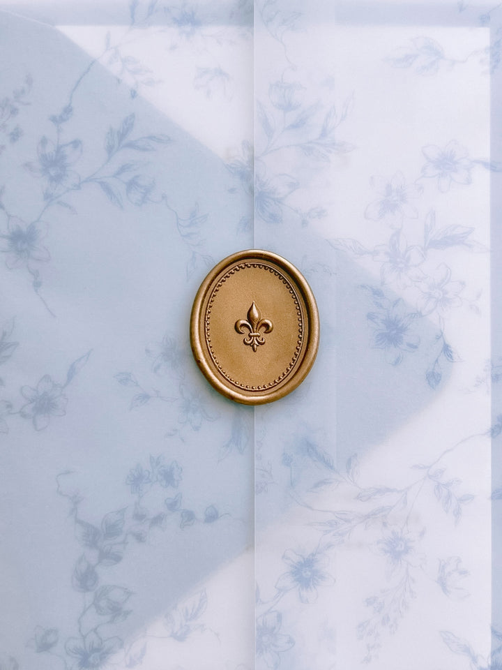 Gold 3D oval fleur-de-lis wax seal on a translucent vellum wedding envelope with a blue floral print