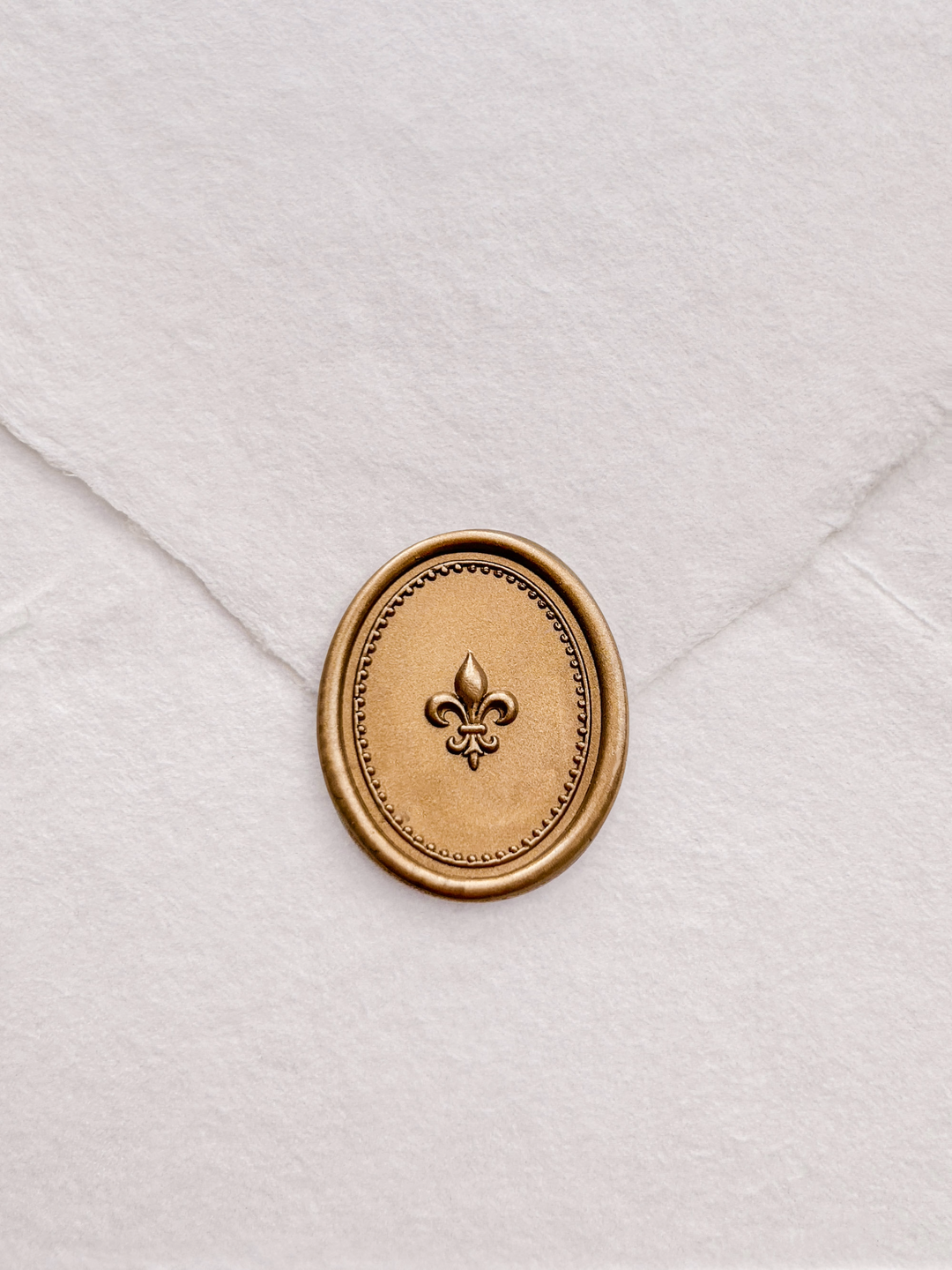 Gold 3D fleur-de-lis oval wax seal on a white deckle-edge handmade paper envelope