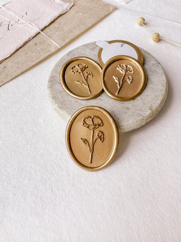 Oval floral wax seals in gold styled with a small gray stone dish, handmade paper and a dried floral branch