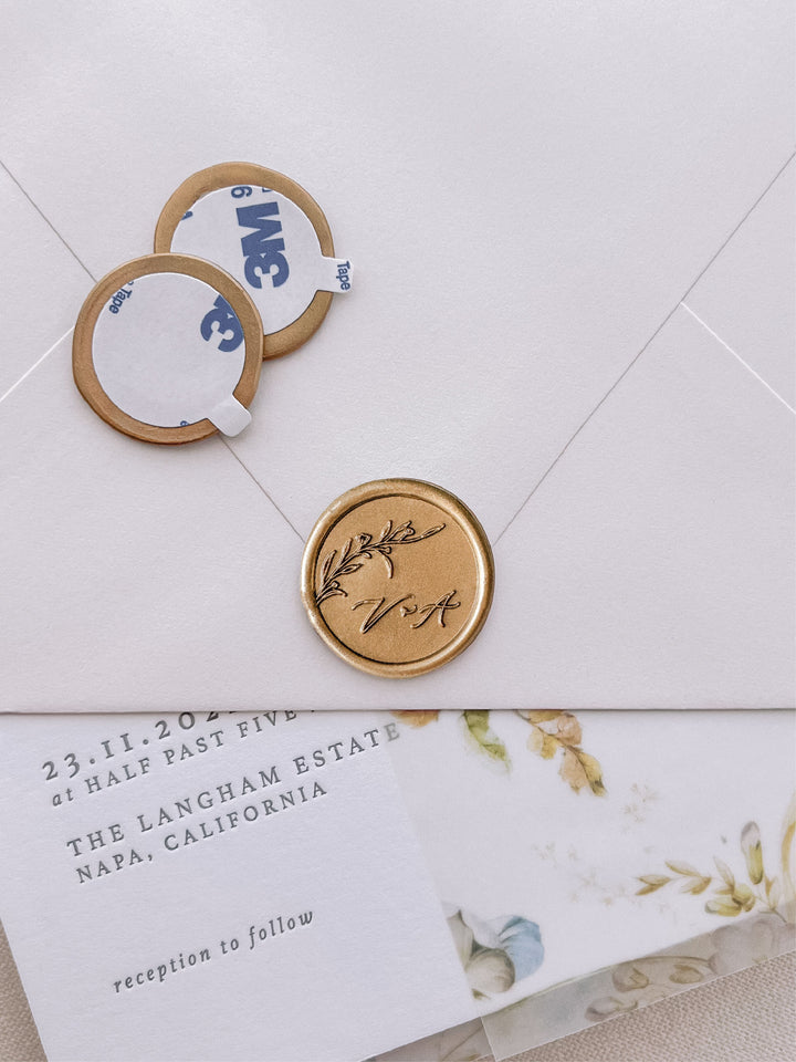 floral branch monogram gold wax seal stickers with self-adhesive backings on a wedding invitation, beige envelope, and floral vellum jacket