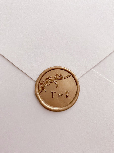 Floral branch monogram wax seal in gold with typeface initials on paper envelope