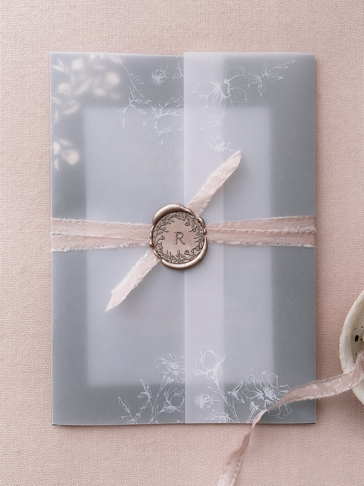 Floral crown single initial mocha custom wax seal on a vellum wrapped wedding invitation in blush silk ribbon