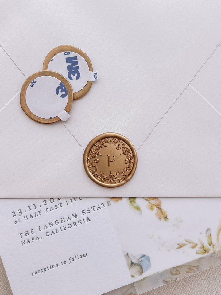 floral crown monogram round gold wax seal stickers with self-adhesive backings on a wedding invitation, beige envelope, and floral vellum jacket
