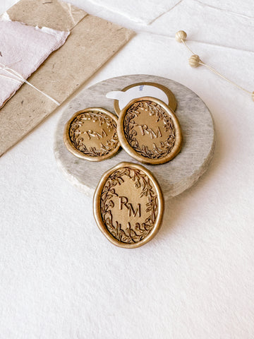 Oval floral crown monogram custom wax seals in gold styled with a small gray stone dish, handmade paper and a dried floral branch