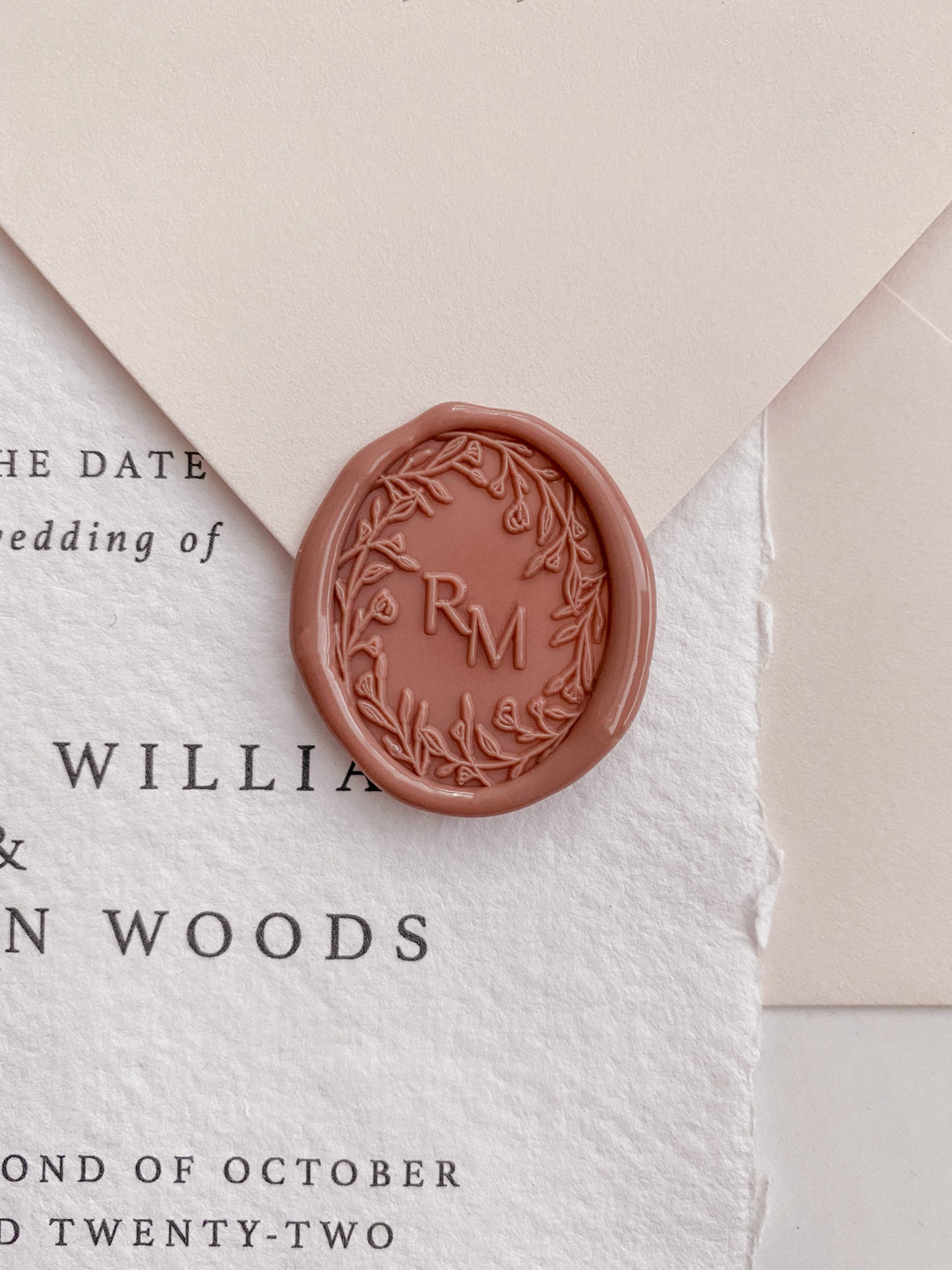 Oval floral crown monogram wax seal in dusty rose on wedding invitation and beige envelope