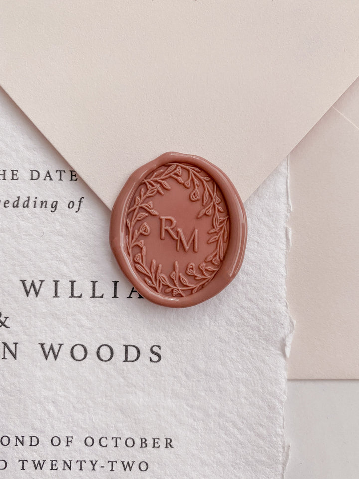 Oval floral crown monogram wax seal in dusty rose on wedding invitation and beige envelope