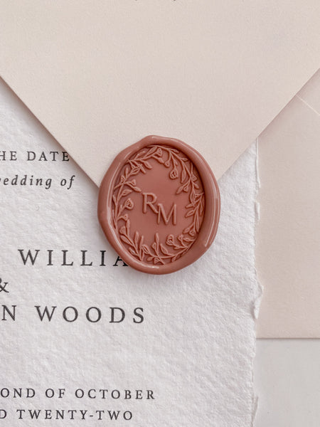 Oval floral crown monogram wax seal in dusty rose on wedding invitation and beige envelope