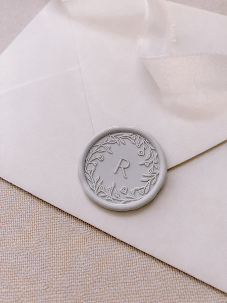 Floral crown single initial custom wax seal in light gray on beige paper enevelope styled with a strand of white silk ribbon
