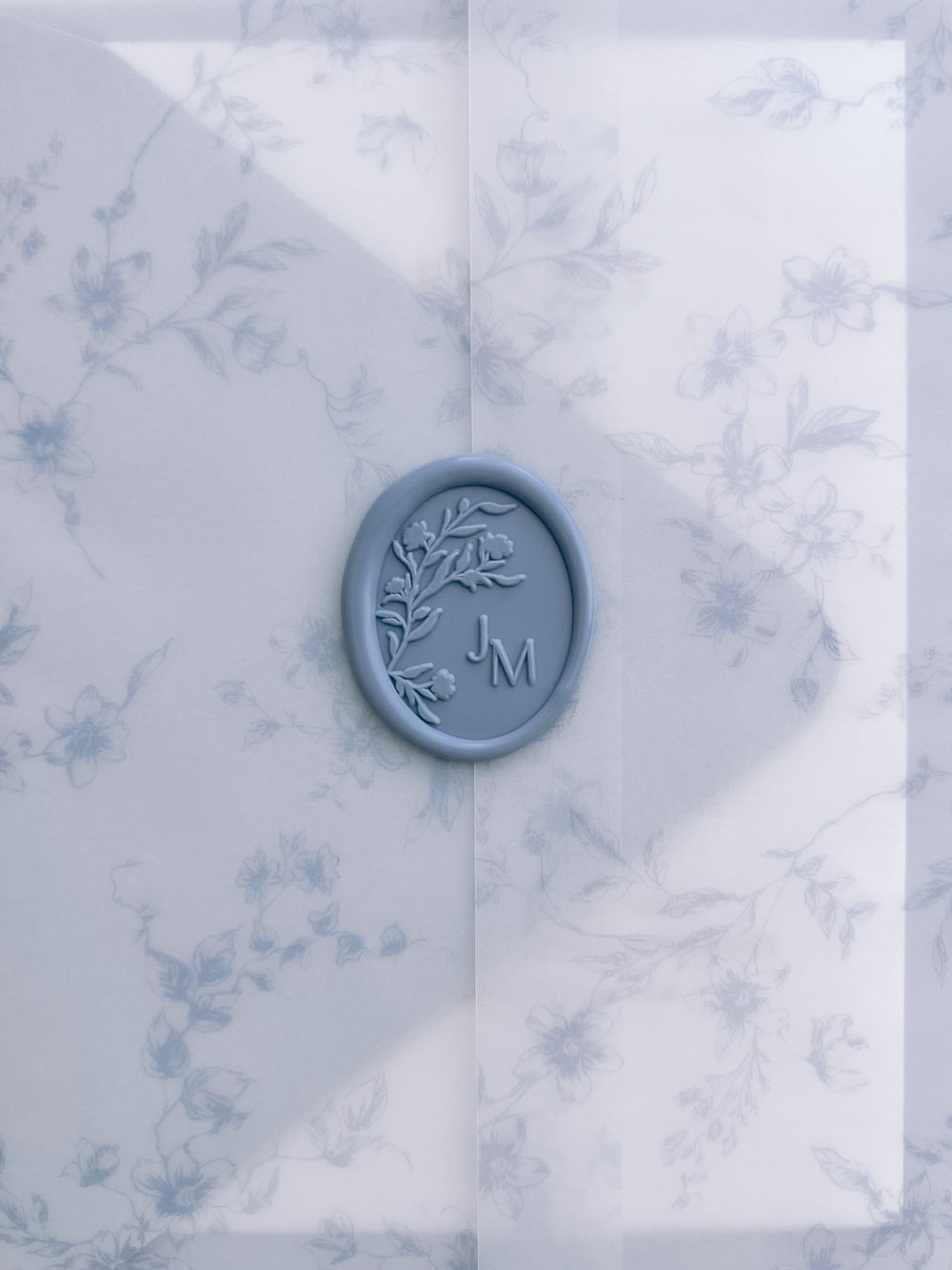 Dusty blue oval floral monogram wax seal with personalized initials on a dusty blue floral print vellum jacket