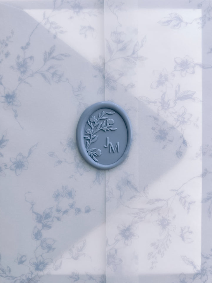 Dusty blue oval floral monogram wax seal with personalized initials on a dusty blue floral print vellum jacket