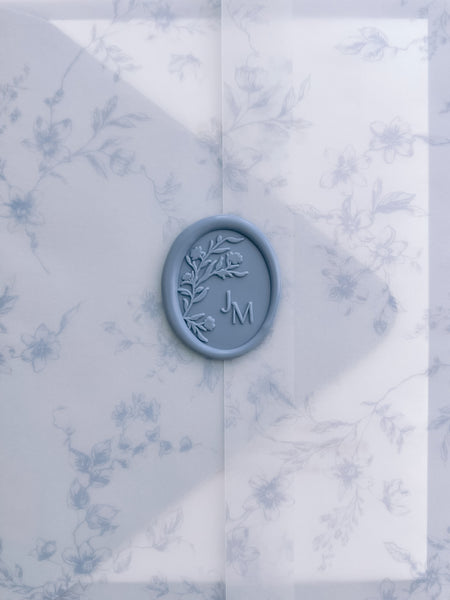 Dusty blue oval floral monogram wax seal with personalized initials on a dusty blue floral print vellum jacket