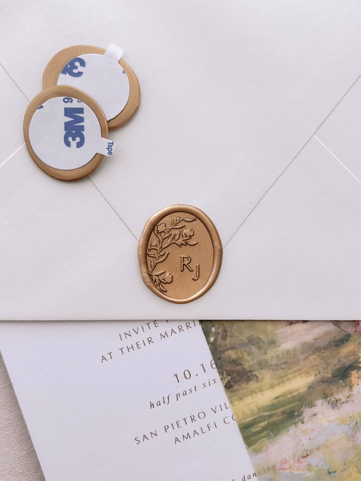 floral silhouette monogram oval gold wax seal stickers with self-adhesive backings on a wedding invitation, beige envelope, and floral vellum jacket