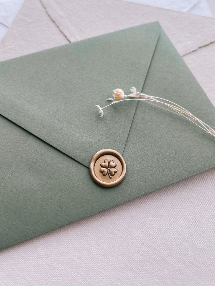 gold four leaf clover mini wax seal on an olive green envelope