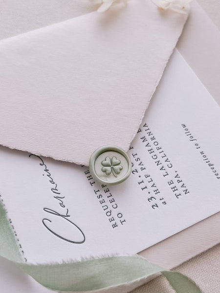 Pearlescent light green four leaf clover wax seal on a wedding invitation card with a light pink envelope