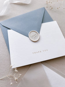 white gold foil thank you card with a dusty blue envelope and white thank you wax seal