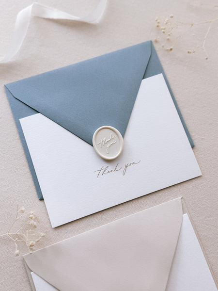 gold foil white thank you card with dusty blue envelope and white thank you wax seal 