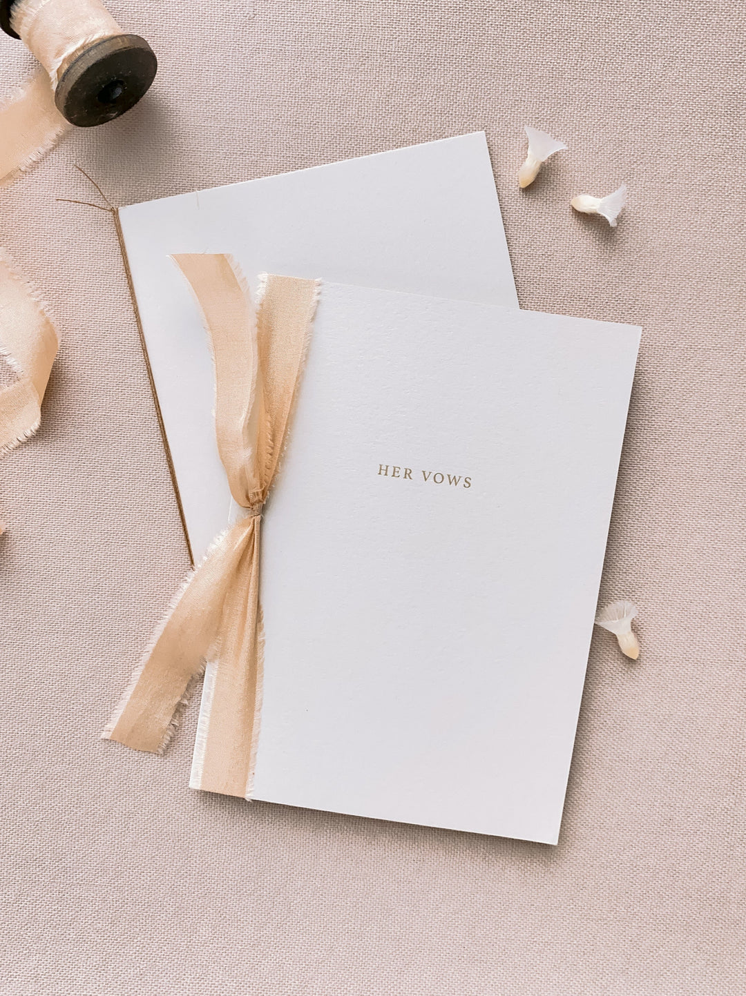 A set of two His and Her gold foil beige card stock vow books in typeface font with one tied in light gold colored silk ribbon and the other in fine brown twine